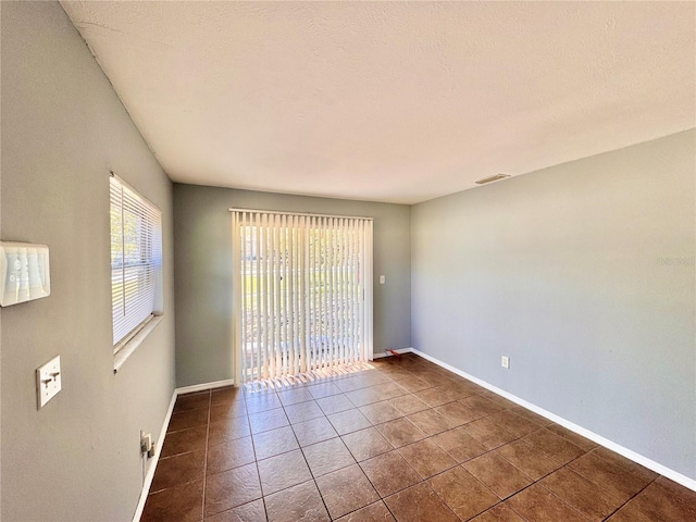 spare room featuring visible vents, a textured ceiling, baseboards, and tile patterned floors