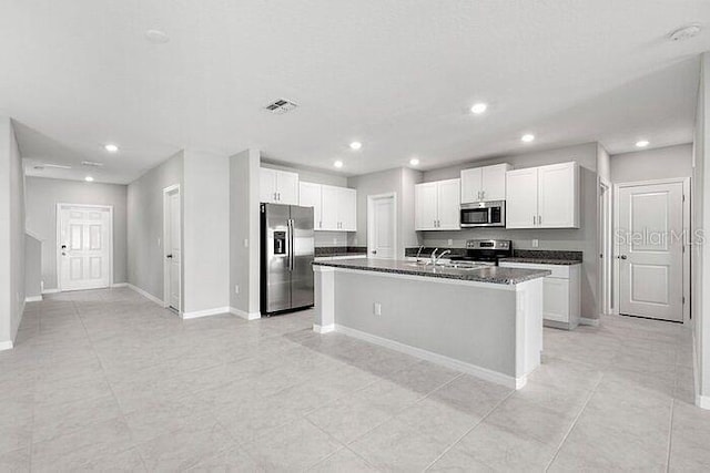 kitchen featuring a center island with sink, appliances with stainless steel finishes, light tile floors, and dark stone counters