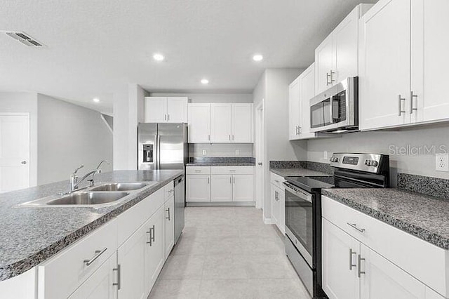 kitchen featuring stainless steel appliances, light tile flooring, an island with sink, white cabinets, and sink