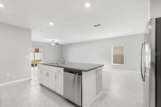 kitchen with appliances with stainless steel finishes, ceiling fan, a center island with sink, light tile flooring, and white cabinetry