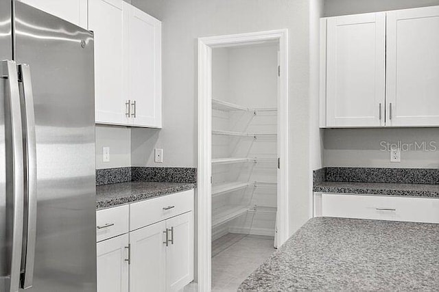 kitchen with dark stone counters, white cabinetry, light tile floors, and stainless steel fridge