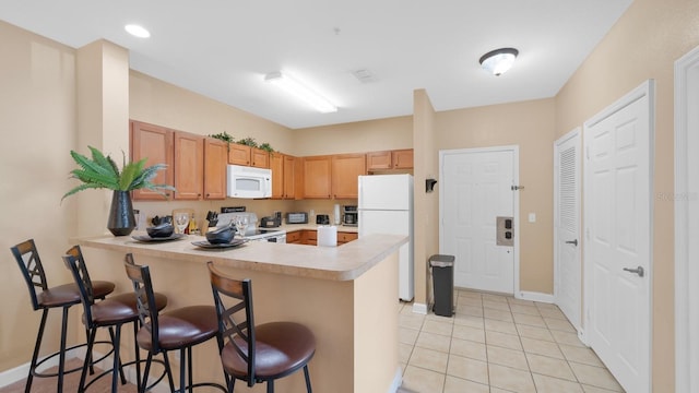 kitchen featuring light tile patterned floors, a kitchen breakfast bar, kitchen peninsula, and white appliances