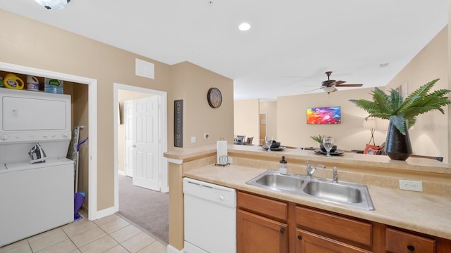 kitchen featuring ceiling fan, stacked washer and dryer, sink, white dishwasher, and light tile patterned floors