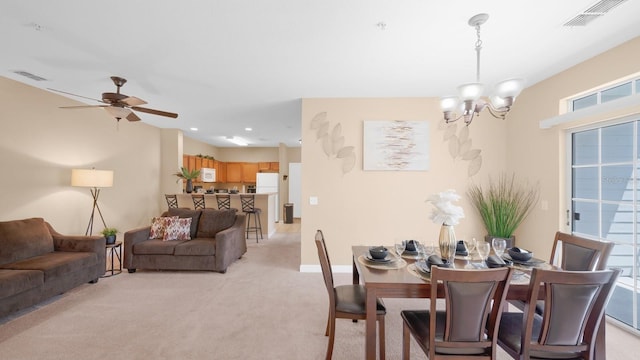 carpeted dining area with ceiling fan with notable chandelier