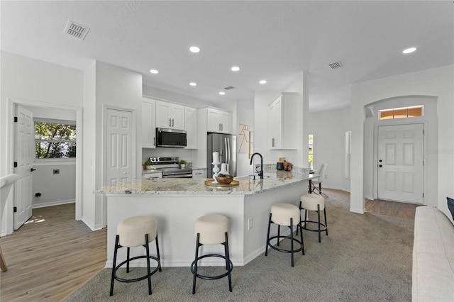 kitchen with appliances with stainless steel finishes, light wood-type flooring, white cabinetry, a breakfast bar area, and light stone countertops