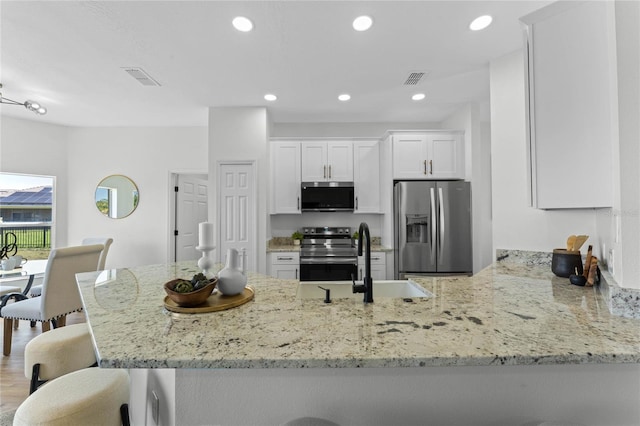 kitchen with light stone counters, appliances with stainless steel finishes, white cabinetry, hardwood / wood-style floors, and kitchen peninsula