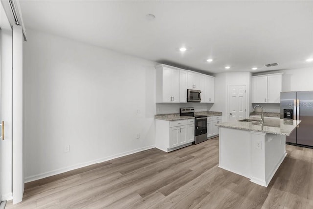 kitchen featuring light wood-type flooring, stainless steel appliances, sink, and an island with sink