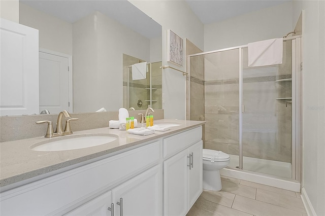 bathroom with a shower with shower door, toilet, vanity with extensive cabinet space, double sink, and tile floors