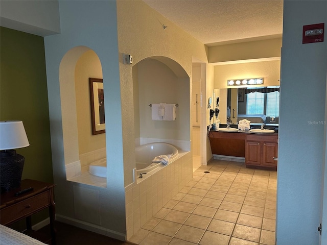 bathroom with a textured ceiling, double vanity, tile flooring, and tiled bath