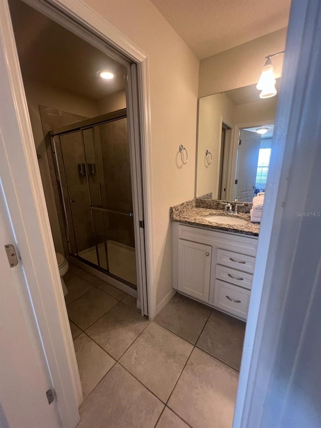 bathroom with vanity with extensive cabinet space, a shower with shower door, toilet, and tile floors