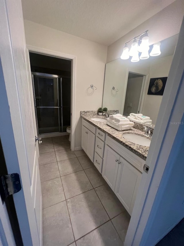 bathroom with a textured ceiling, toilet, tile floors, and dual vanity