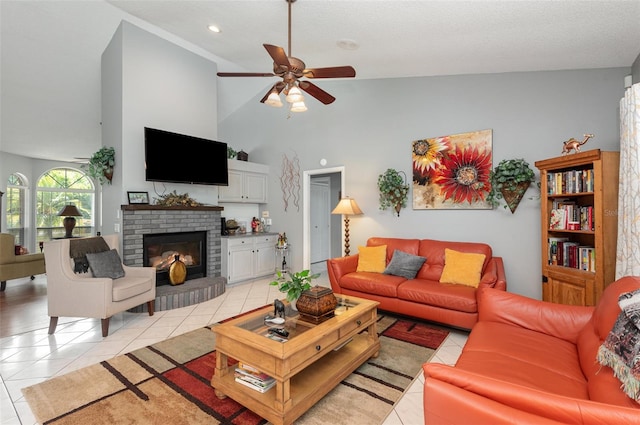 living room featuring high vaulted ceiling, a fireplace, light tile flooring, ceiling fan, and a textured ceiling