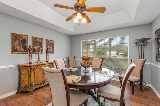 dining area with a textured ceiling, ceiling fan, hardwood / wood-style floors, and a tray ceiling