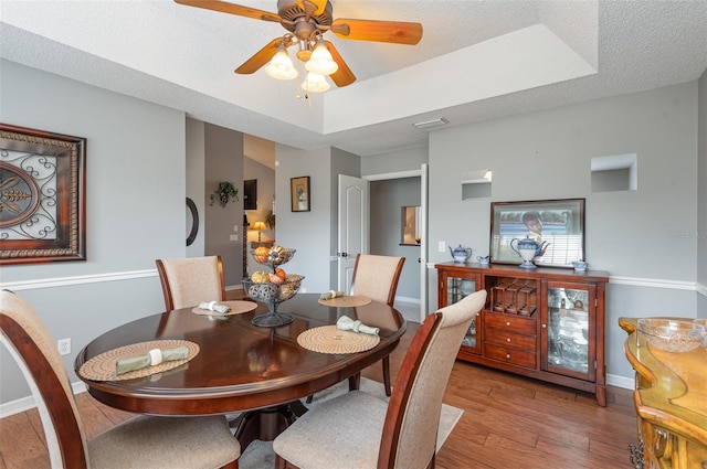 dining room featuring hardwood / wood-style floors, ceiling fan, a tray ceiling, and a textured ceiling