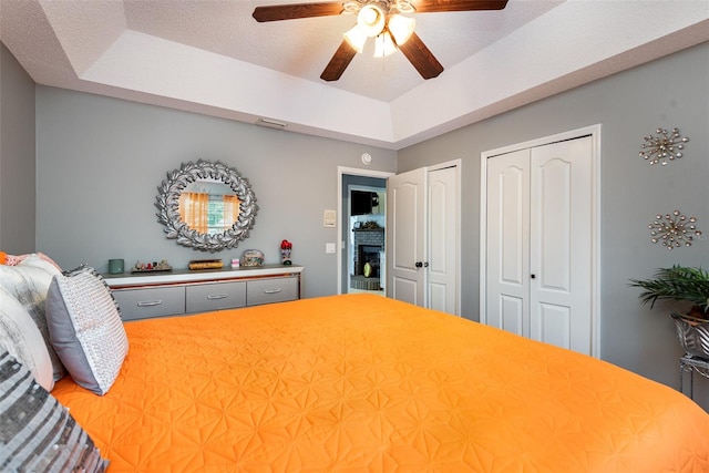 bedroom featuring two closets, ceiling fan, a tray ceiling, and a textured ceiling