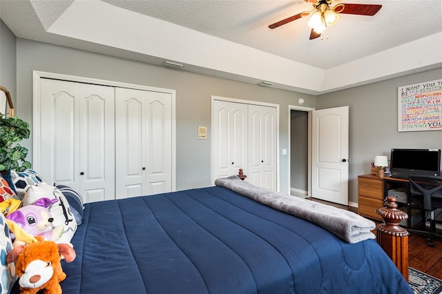 bedroom featuring multiple closets, dark hardwood / wood-style floors, ceiling fan, and a textured ceiling