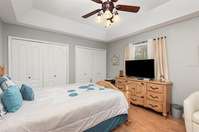 bedroom featuring light hardwood / wood-style floors, ceiling fan, a tray ceiling, and multiple closets