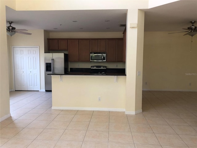 kitchen featuring stainless steel appliances, a kitchen bar, light tile patterned floors, and kitchen peninsula