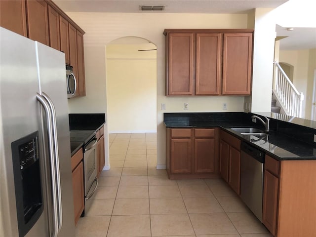 kitchen featuring stainless steel appliances, sink, light tile patterned floors, and dark stone counters