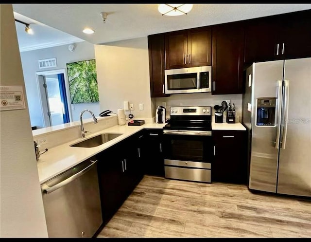 kitchen featuring stainless steel appliances, dark brown cabinets, sink, crown molding, and light wood-type flooring