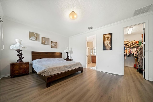 bedroom featuring crown molding, connected bathroom, a spacious closet, wood-type flooring, and a closet