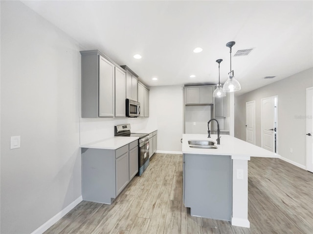 kitchen with sink, light hardwood / wood-style floors, hanging light fixtures, stainless steel appliances, and an island with sink