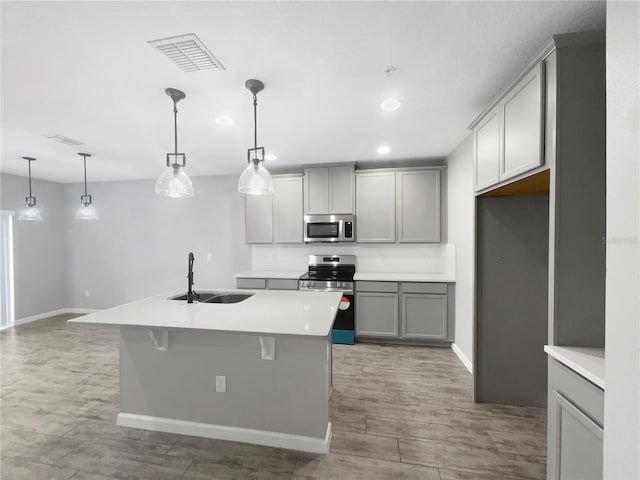 kitchen featuring decorative light fixtures, a center island with sink, appliances with stainless steel finishes, and sink