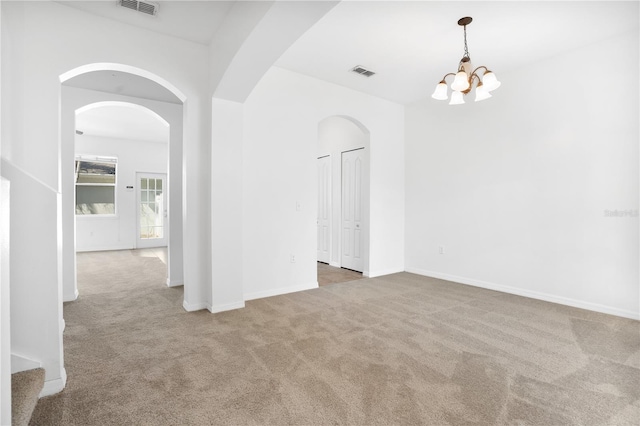 carpeted spare room featuring arched walkways, visible vents, a notable chandelier, and baseboards