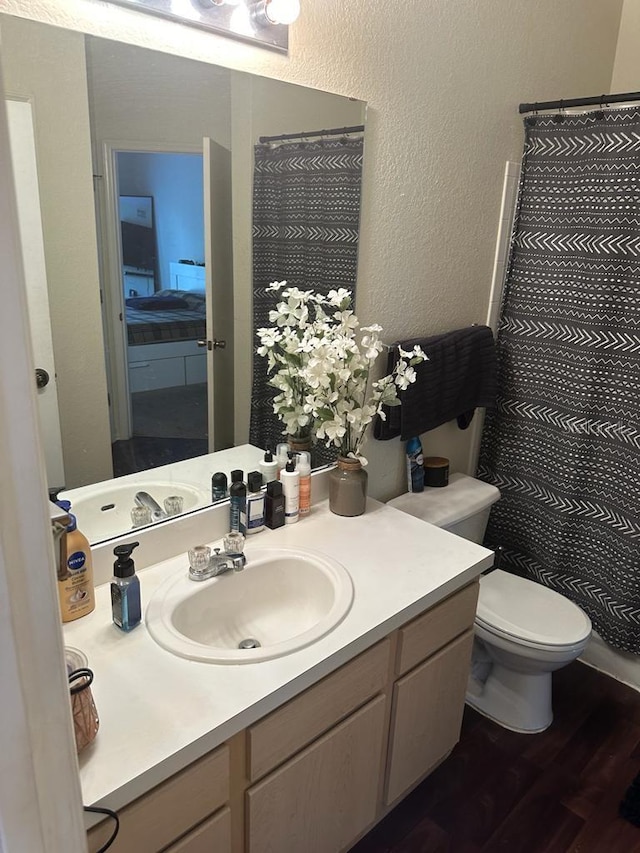 bathroom featuring vanity with extensive cabinet space, toilet, and wood-type flooring