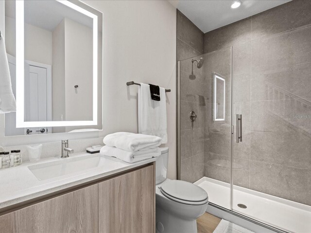 bathroom featuring a shower with door, wood-type flooring, vanity, and toilet