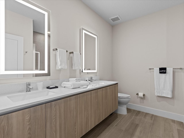 bathroom with vanity with extensive cabinet space, double sink, toilet, and hardwood / wood-style floors