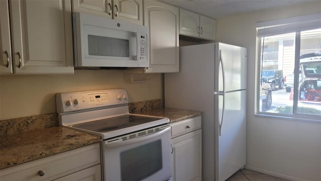 kitchen with white cabinets, white appliances, light tile flooring, and stone countertops