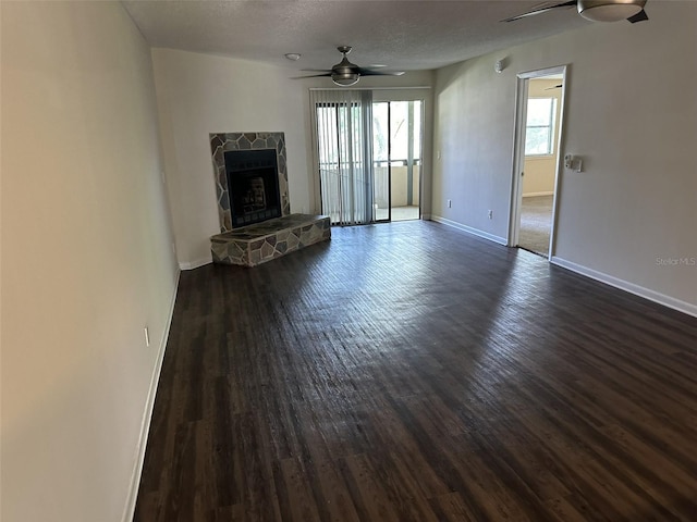 unfurnished living room with a textured ceiling, ceiling fan, a fireplace, and dark wood-type flooring