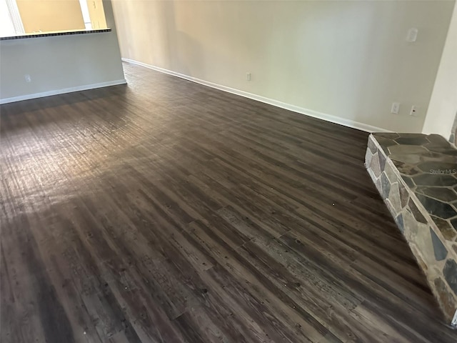 unfurnished room with a stone fireplace and dark wood-type flooring