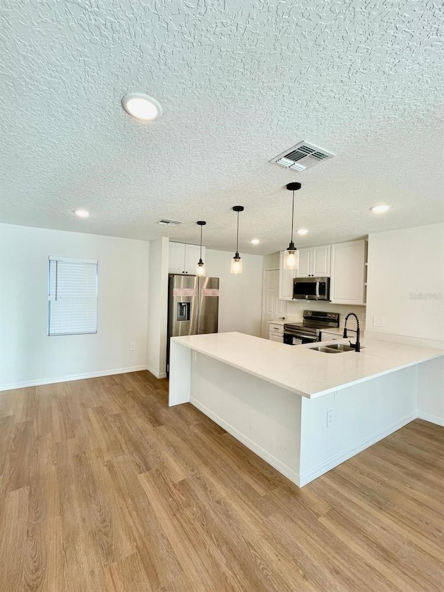 kitchen with appliances with stainless steel finishes, pendant lighting, light hardwood / wood-style floors, and white cabinetry