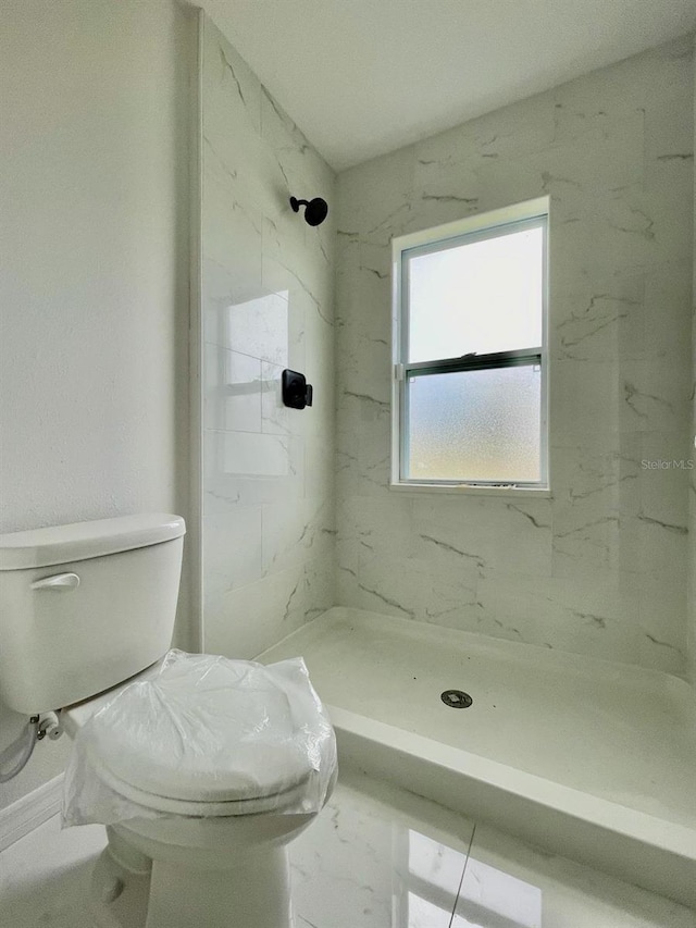 bathroom with tile floors, toilet, and tiled shower