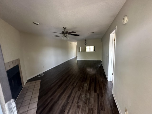 unfurnished living room featuring dark hardwood / wood-style floors, ceiling fan, a tile fireplace, and a textured ceiling