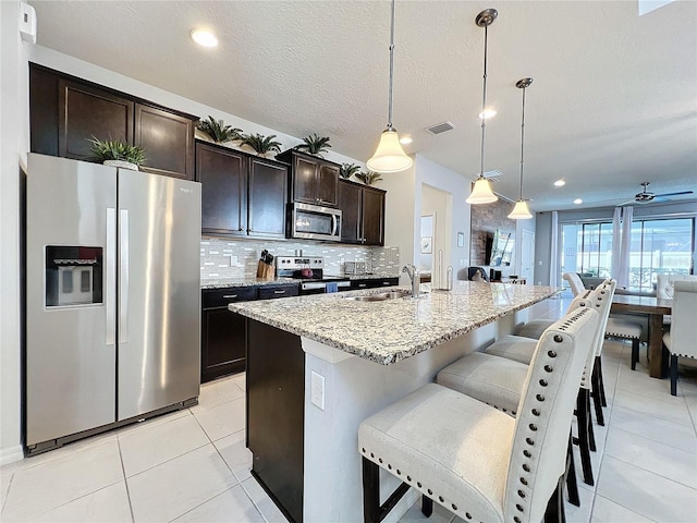 kitchen featuring light tile flooring, stainless steel appliances, sink, tasteful backsplash, and an island with sink