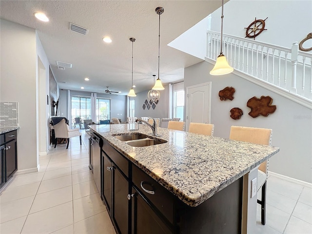 kitchen with a kitchen bar, sink, an island with sink, and hanging light fixtures