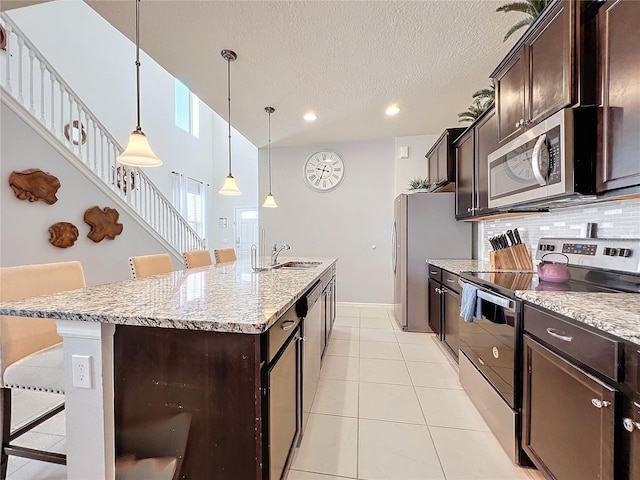 kitchen featuring appliances with stainless steel finishes, tasteful backsplash, a breakfast bar area, a center island with sink, and pendant lighting