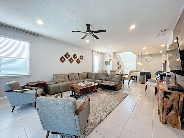 tiled living room featuring ceiling fan with notable chandelier and a textured ceiling