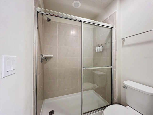 bathroom featuring a shower with shower door and toilet