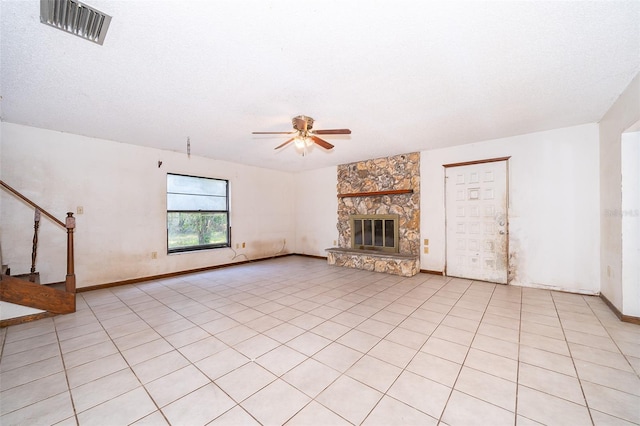 unfurnished living room featuring a stone fireplace, a textured ceiling, light tile patterned floors, and ceiling fan