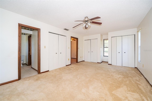 unfurnished bedroom with multiple closets, a textured ceiling, light colored carpet, and ceiling fan