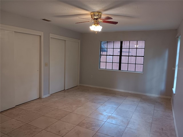 unfurnished bedroom with ceiling fan, light tile floors, and multiple closets