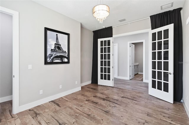 unfurnished room featuring hardwood / wood-style floors, french doors, and a chandelier