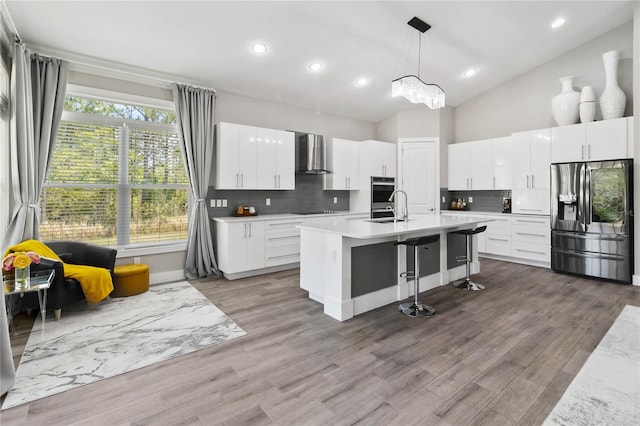 kitchen featuring wall chimney exhaust hood, stainless steel appliances, white cabinets, and backsplash