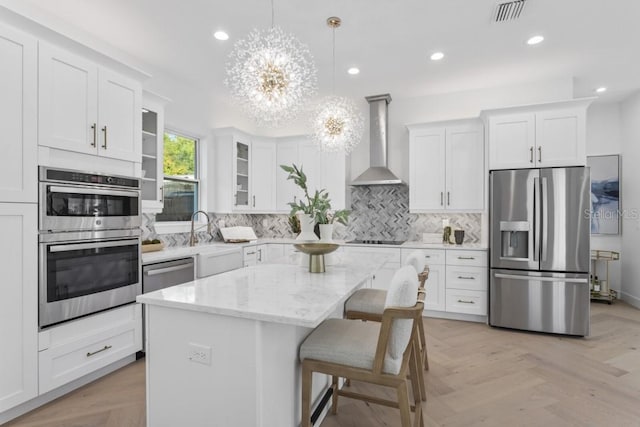 kitchen with light parquet floors, stainless steel appliances, white cabinetry, a center island, and wall chimney exhaust hood