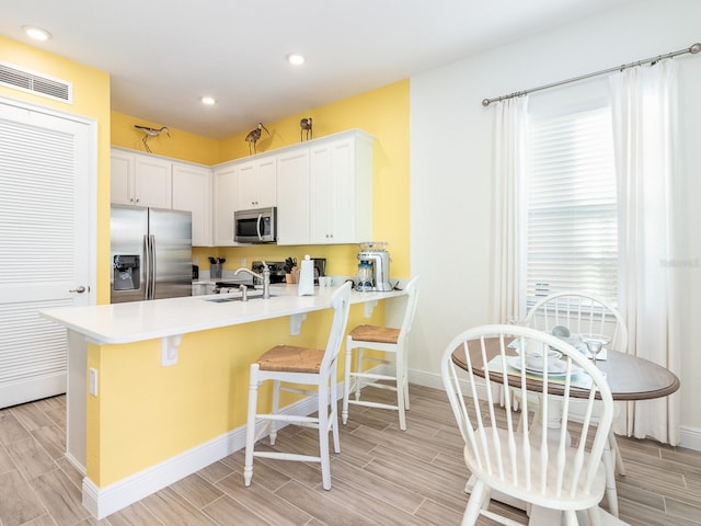 kitchen with white cabinetry, kitchen peninsula, appliances with stainless steel finishes, a kitchen bar, and sink