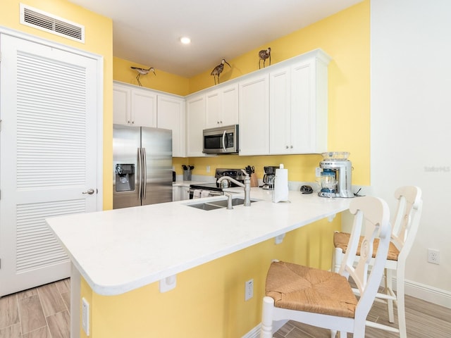 kitchen with appliances with stainless steel finishes, kitchen peninsula, a breakfast bar, and white cabinetry